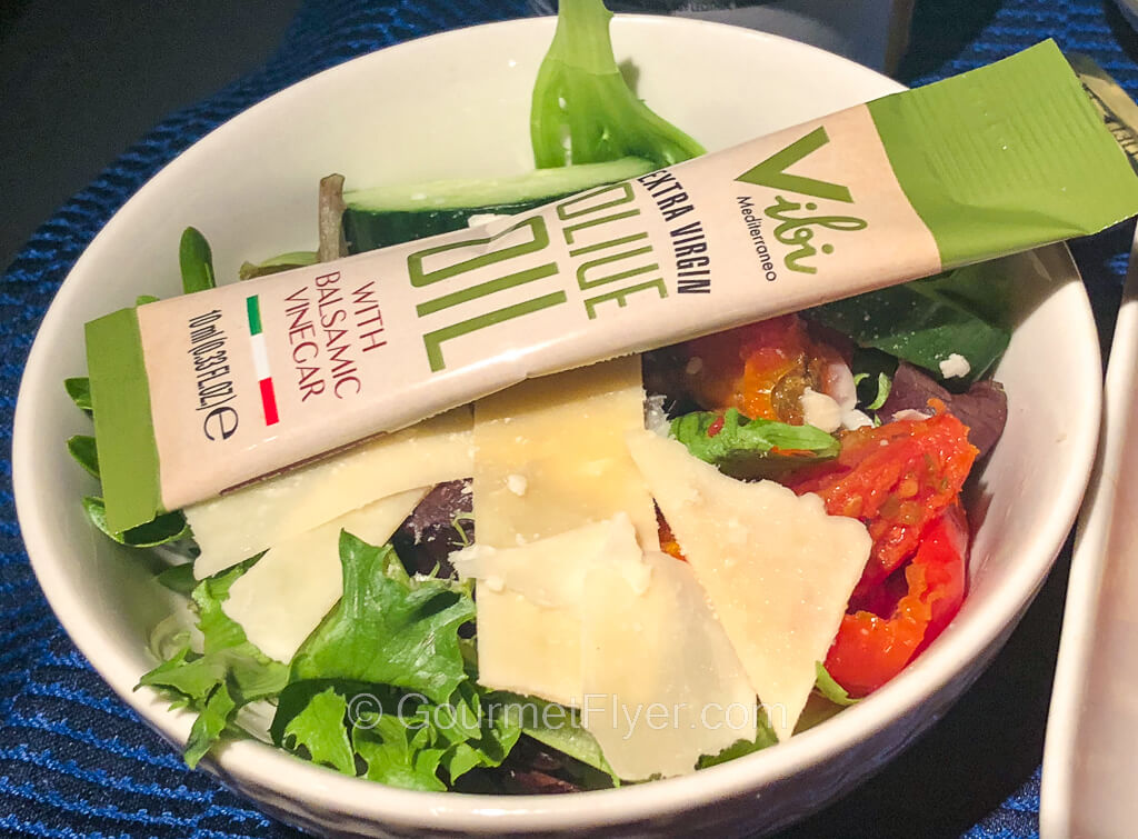 A green salad is topped with cheese and a packet of olive oil dressing.