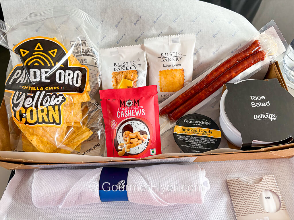 A snack box is opened up to display its contents of various packaged snacks, chips, an jerkies.