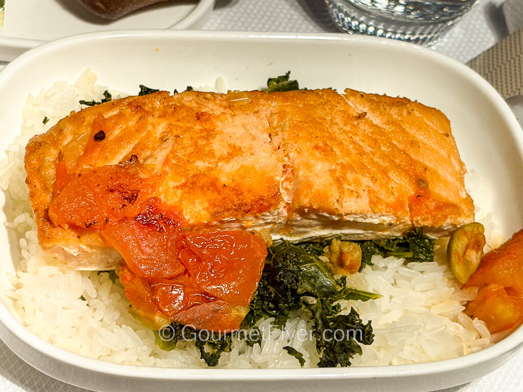 A piece of grilled fish is served on a plate with rice and green vegetables.