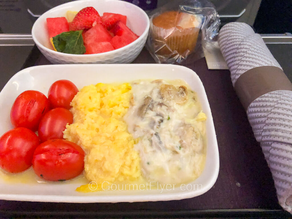 A dish of scrambled eggs in a white cream sauce is accompanied by a side of cherry tomatoes.