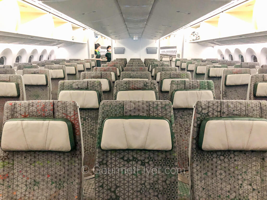 Sets of airline seats in sections of threes are seen from the front of the cabin looking toward the back.