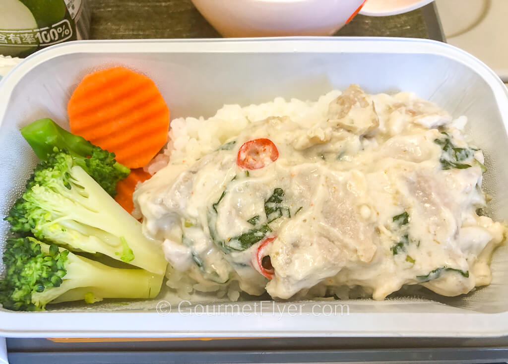 A rectangular bowl contains a creamy meat over rice, broccoli, and carrots.