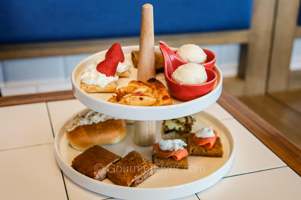 A two-tiered tray contains a variety of savory and sweet snacks and finger foods.