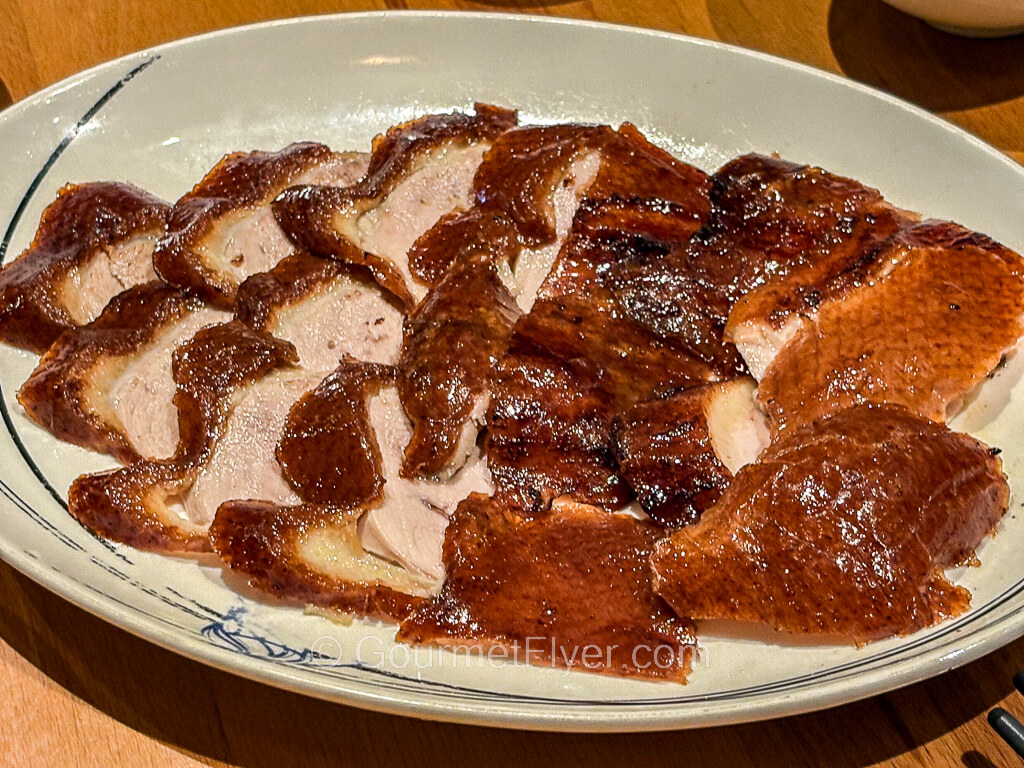 Thinly sliced dick meat with a golden-brown skin is layered and served on a long porcelain plate.