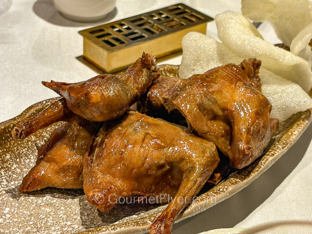 A fried squab cut into four quarters is served on a plate garnished with prawn chips.