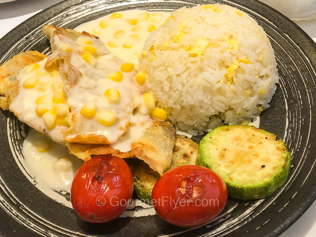 A piece of grilled fish filet covered in plenty of creamed corn sauce is served with a side of fried rice.