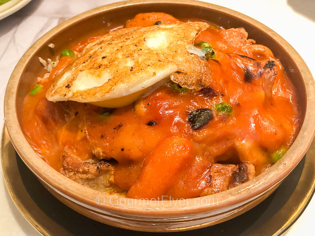 A round casserole of baked food is covered in a red sauce and topped with a fried egg.