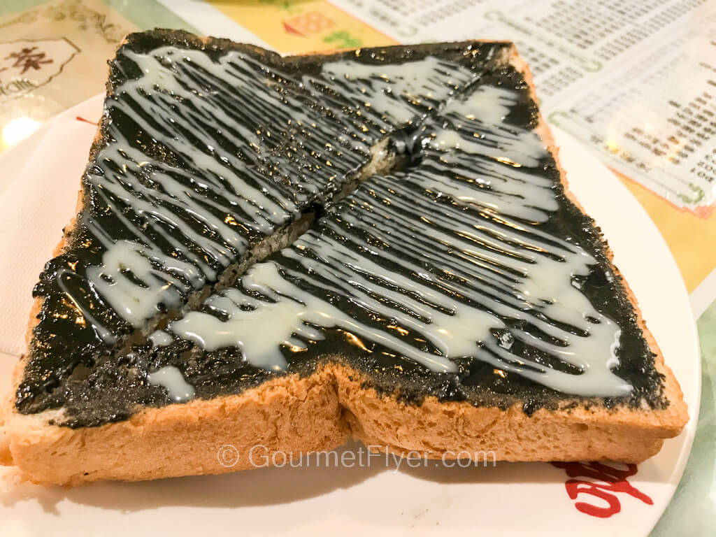 A slice of bread is topped with a black paste crisscrossed with a white sauce.