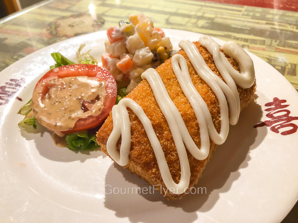 A shrimp toast is topped with mayonnaise and served with a side of potato salad. 