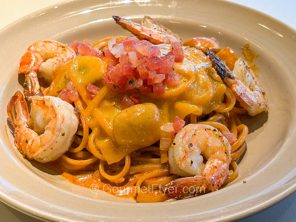 Several large shrimps sit atop a plate of pasta tossed in a creamy red sauce.