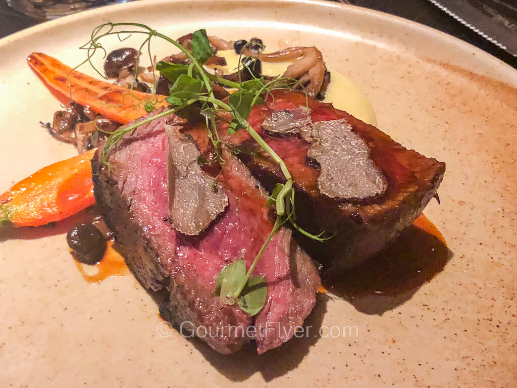 A steak is cut in halves to show its medium rare center garnished with truffles.