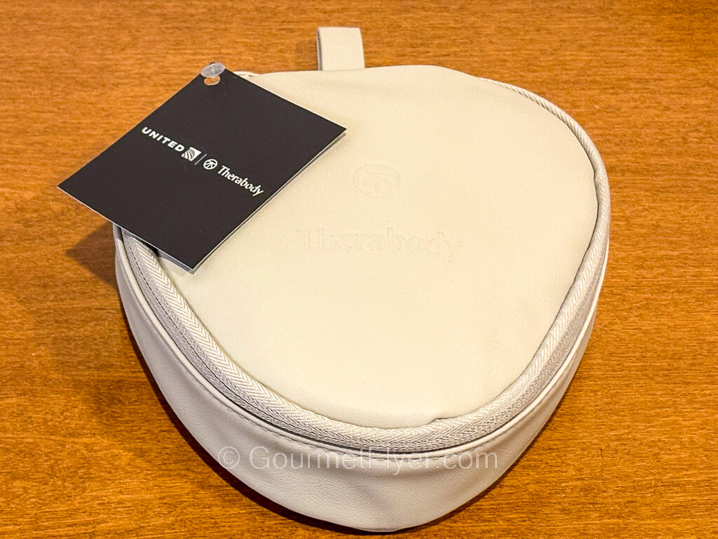 A small light gray color leather travel case has a tag with United and Therabody logos.