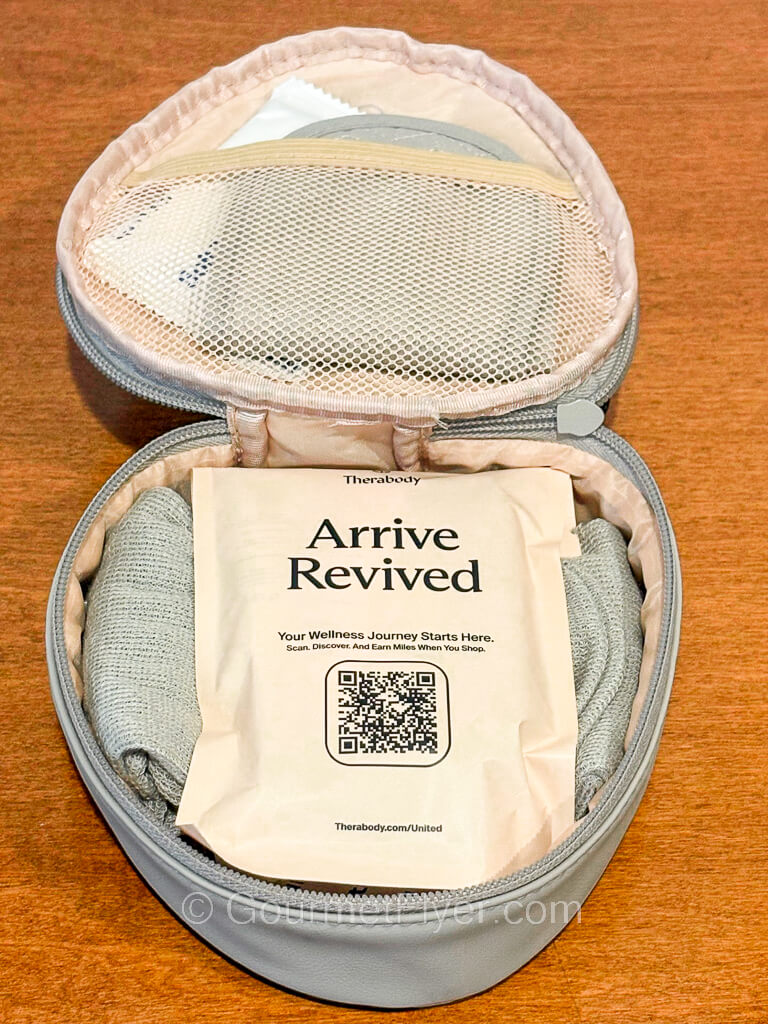 A light gray color small travel case is opened to reveal its contents, which include an eye mask in a pocket and a cosmetic package placed on top.