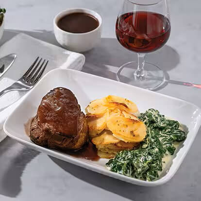 A steak with potatoes and vegetables is accompanied by a glass of red wine.