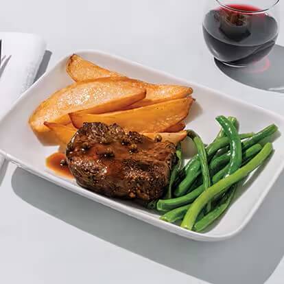 A steak is covered in a brown peppercorn sauce with sides of green beans and potatoes.