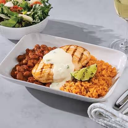 A plate contains a chicken breast filet covered in a white sauce accompanied by Spanish rice and beans.