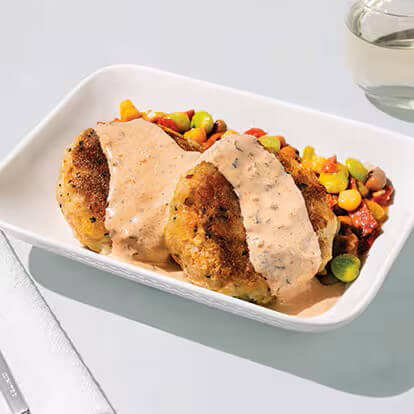 Two pieces of crab cakes are covered in a creamy sauce and accompanied by a blend of vegetables.