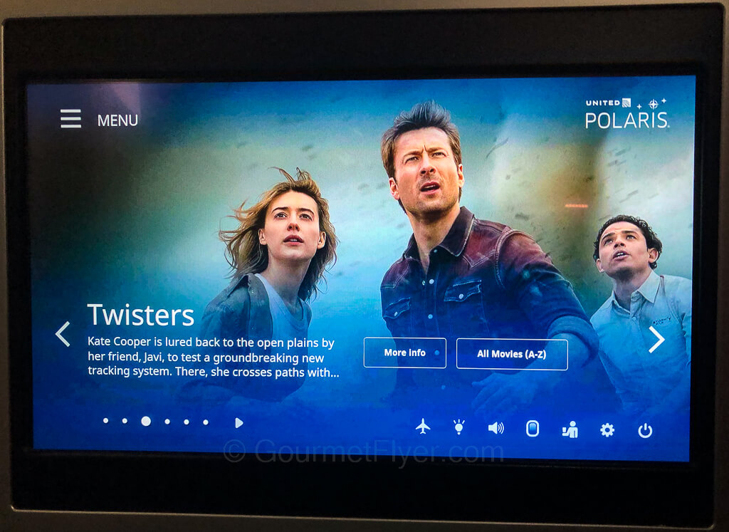 The seatback TV screen of an aircraft displays a screenshot of the characters of the movie Twisters