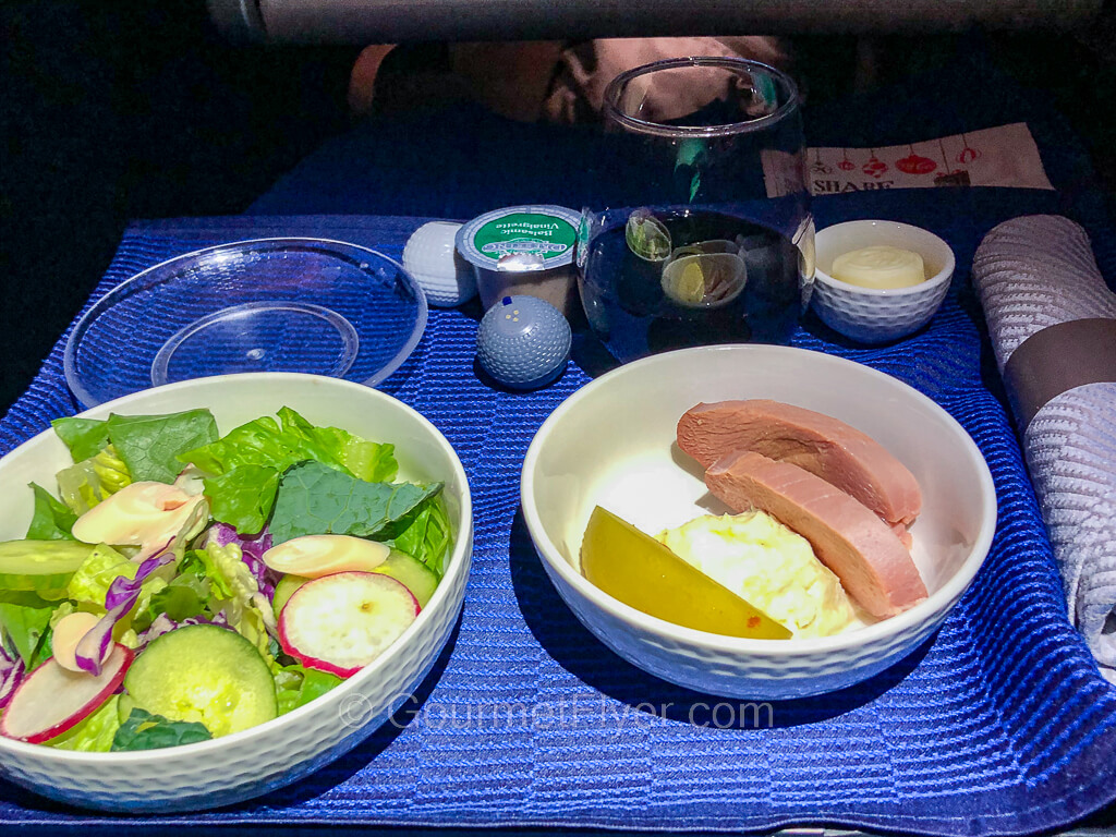 A business class dinner tray contains a meat dish with a side green salad and a glass of red wine.