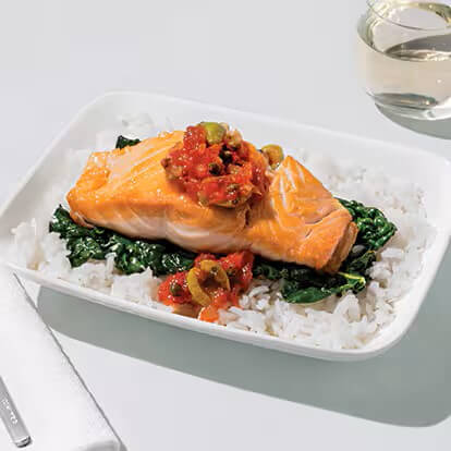 A thick salmon filet sits atop a bed of white rice in a serving dish.