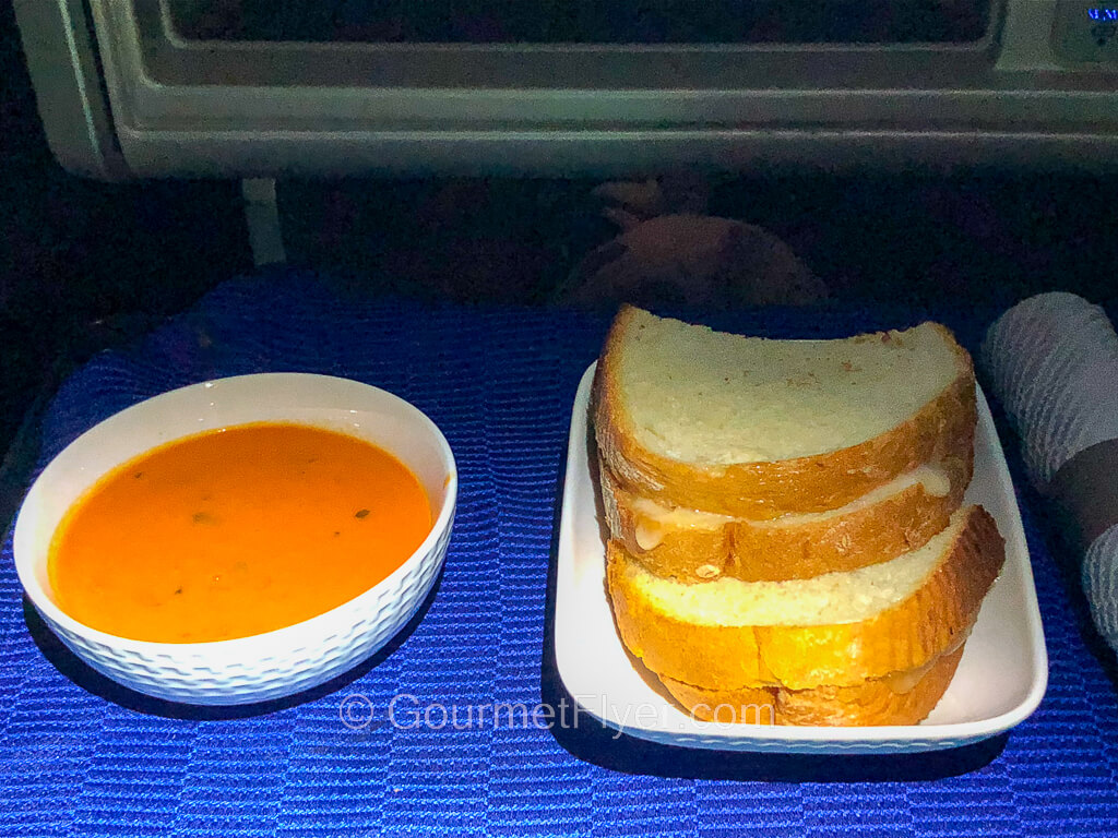 A plate with two sandwiches stacked on top of each other is accompanied by a bowl of tomato soup.