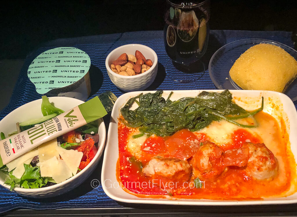 United's regional signature cuisines feature a dish of meatballs in tomato sauce accompanied with a salad, roll, and dessert in a cup.