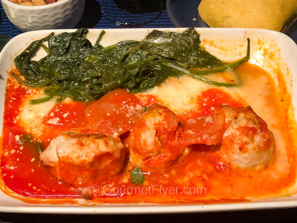 A dish of meatballs covered in a tomato sauce and served with a side of green leafy vegetables.