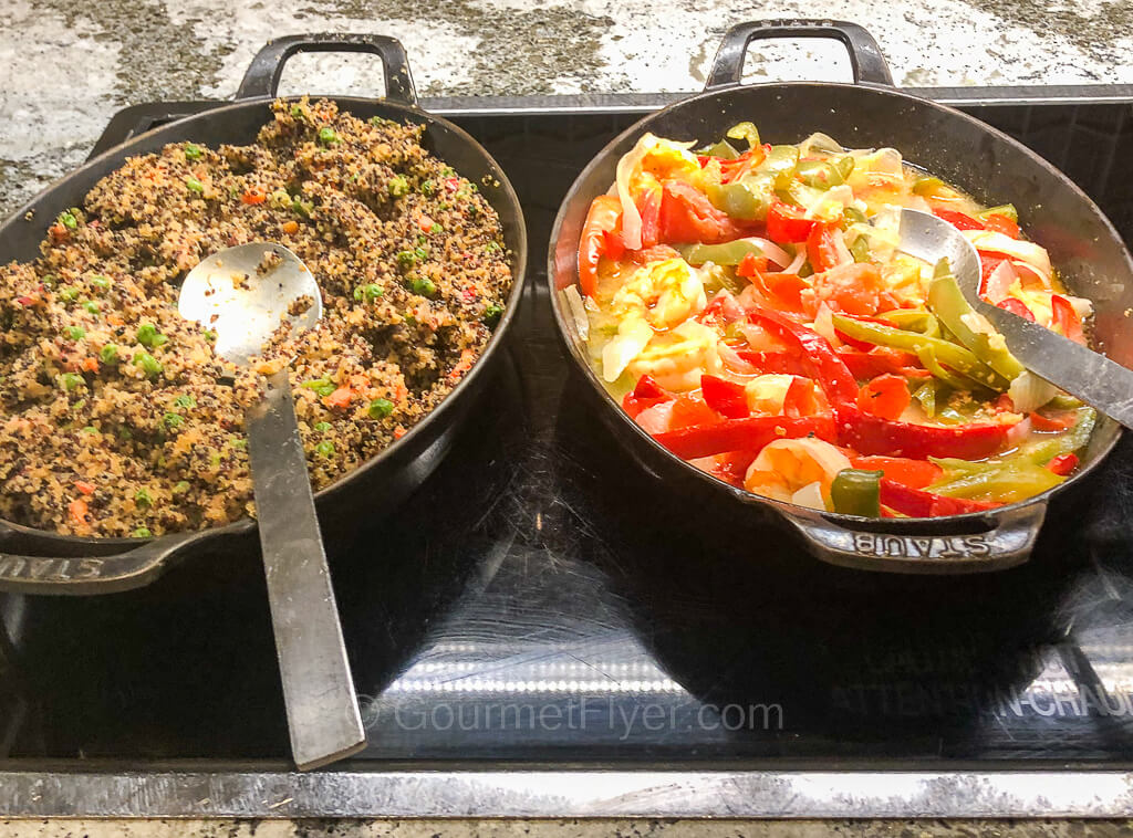 A pot on the right contains a colorful blend of red and green peppers in a yellowish sauce while a pot on the left contains quinoa with vegetables.