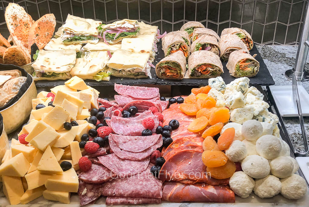 A cheese and deli meat platter is accompanied by cut sandwiches and wraps.