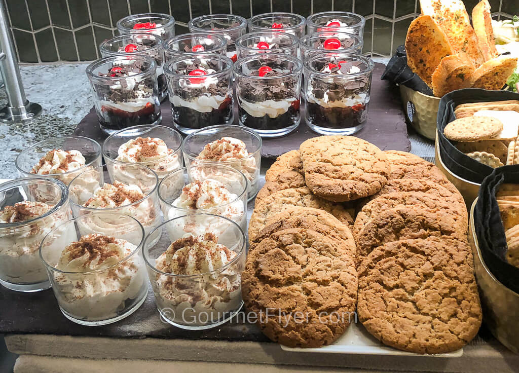 A dessert station contains small cups of mousses and a plate full of cookies.