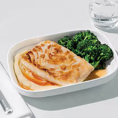 A piece of grilled fish sits atop a bed of mashed potatoes and a side of green vegetables.