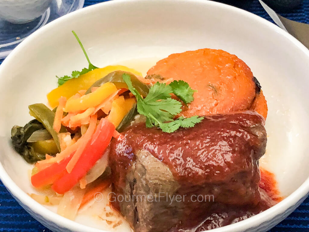 A thick slab of beef is topped with a thick brown gravy and accompanied by sides of vegetables.