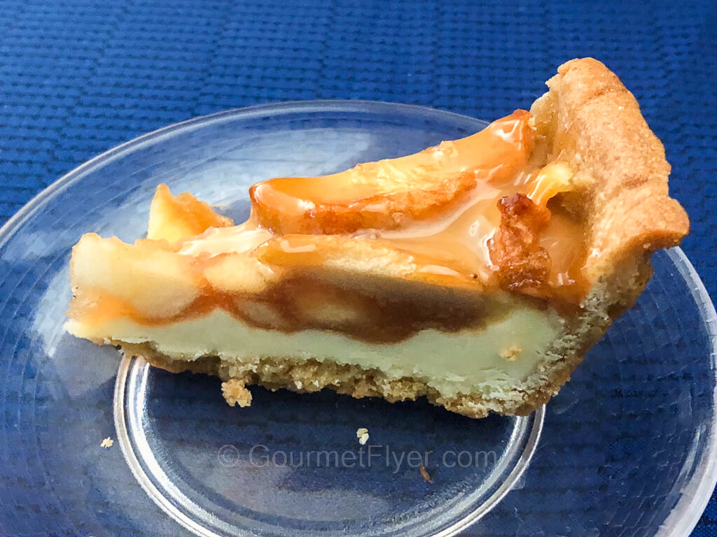 A slice of cheesecake is served on a small plate atop a table in blue tablecloth.