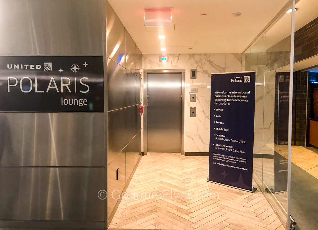 The entrance to United's Polaris Lounge features a prominent sign and a short pathway to an elevator.