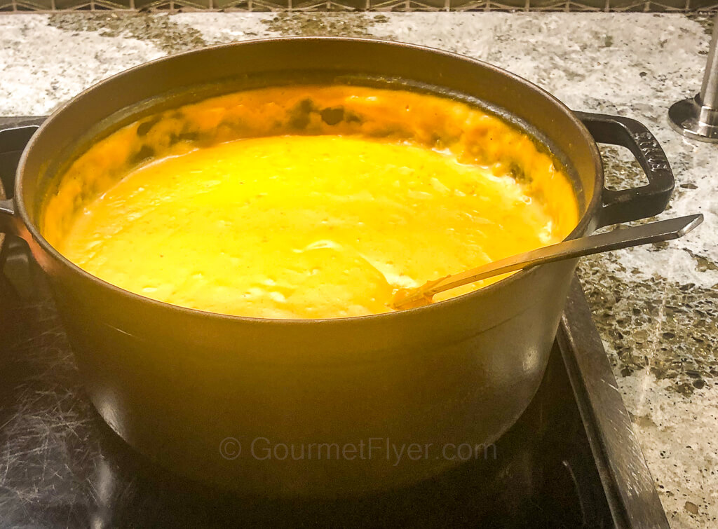 A metal pot on top of a counter contains a creamy looking yellowish soup.