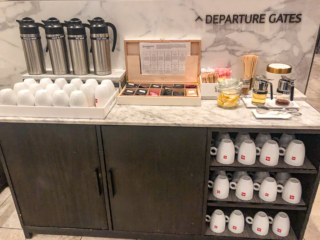 An array of cups are stored in a cabinet which serves plenty of coffee and tea options on its countertop.