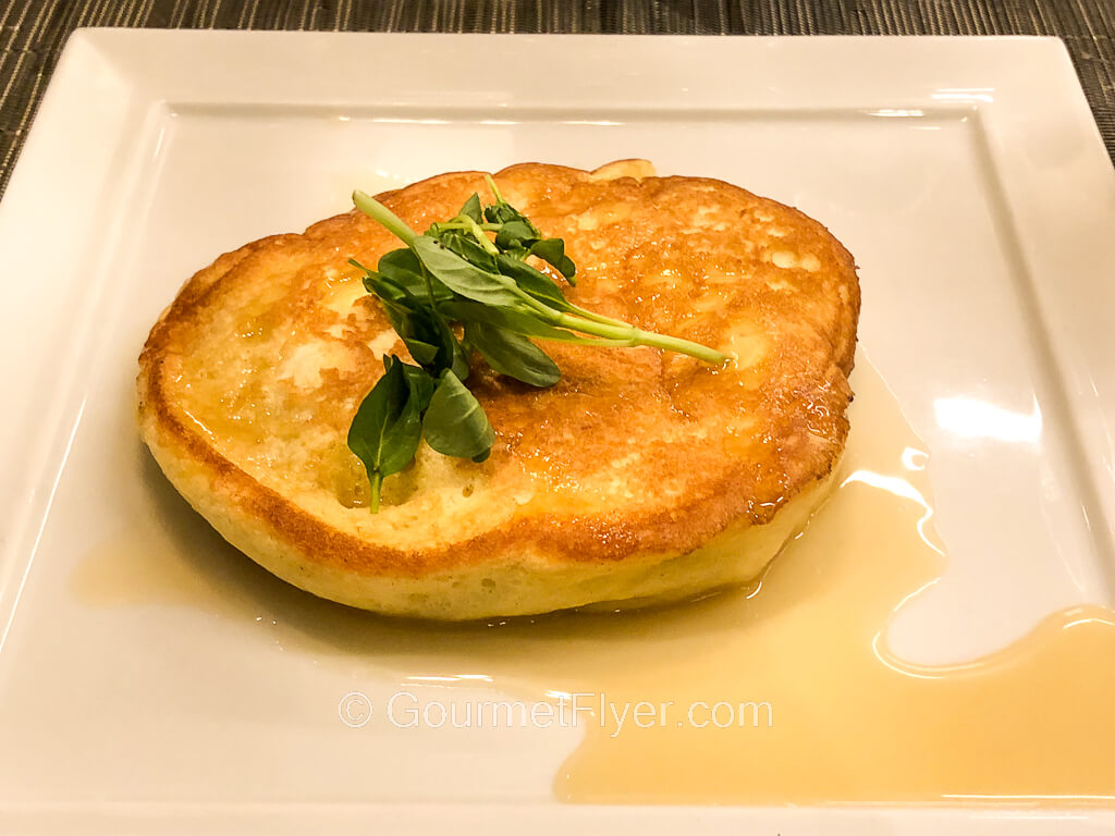 A pancake is garnished with a mint leaf on top and accompanied with a light sauce.