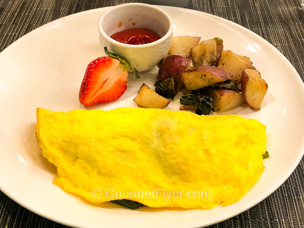 An omelet is served on a plate with a side of potatoes and garnished with a half strawberry.