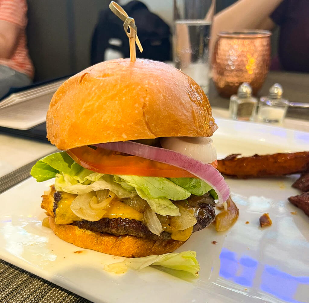 A burger is topped with lettuce, tomatoes, cheese, and onion.