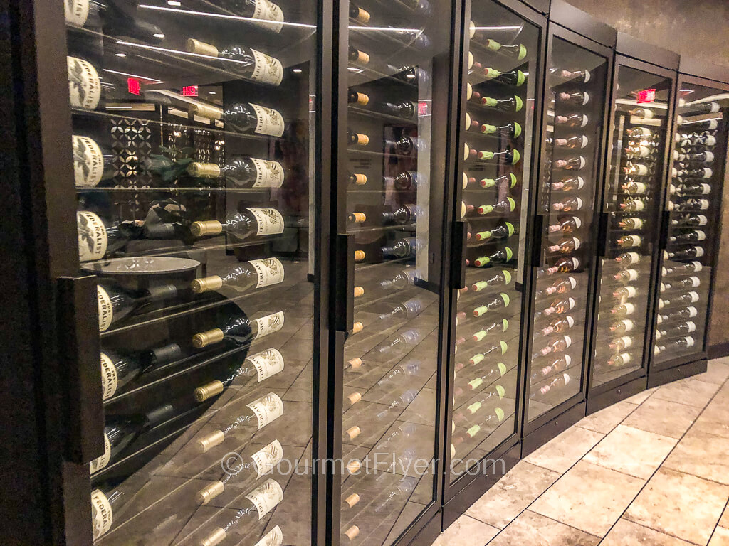 A series of wine cabinets with glass doors line against a curved wall displaying dozens of bottles of wines.