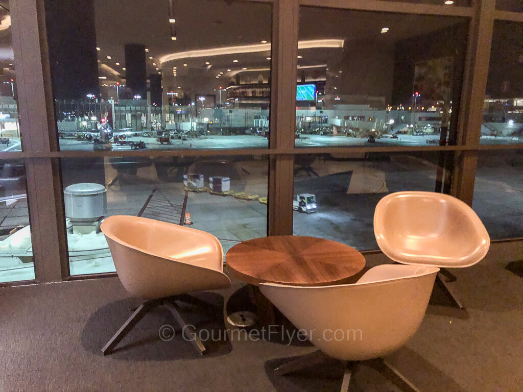 Three trendy looking chairs are accompanied by a small round coffee table next to a window looking over the tarmac.