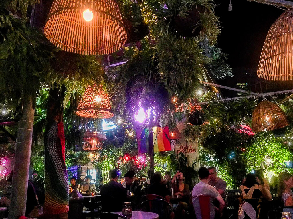 Customers hangout in a crowded cocktail lounge dimly lit with colorful lights.