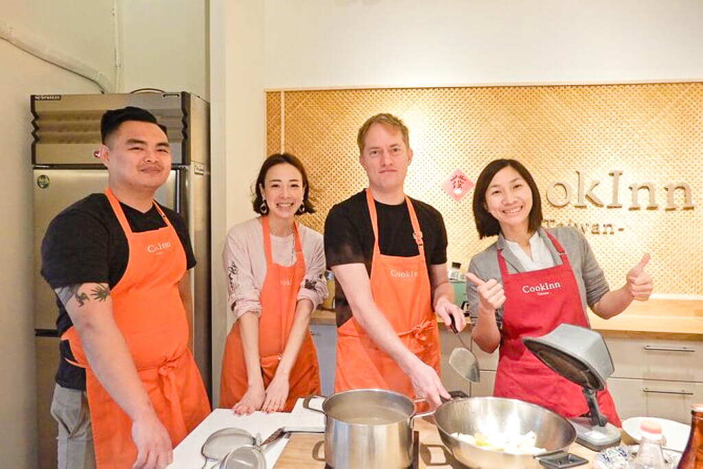 Two men and two women wearing aprons participate in a cooking class.