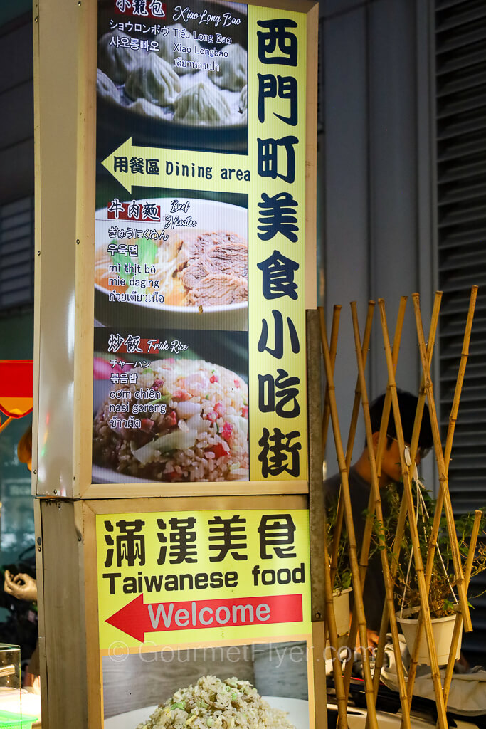 A large, tall lighted sign with pictures points to a food hall to the left of the road.