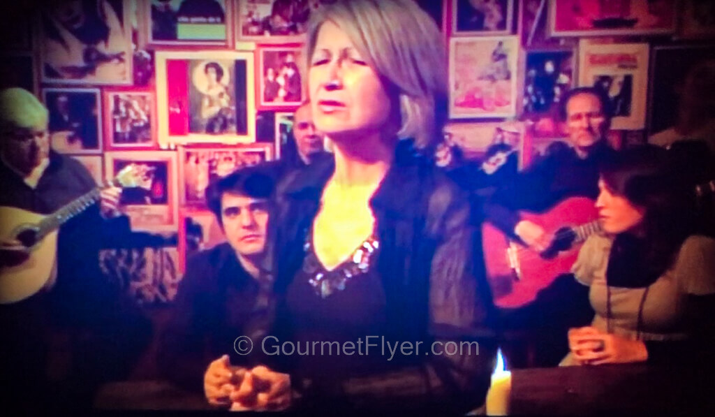 A female singer performs emotionally in front of a band on a stage with many memorabilia in the background.