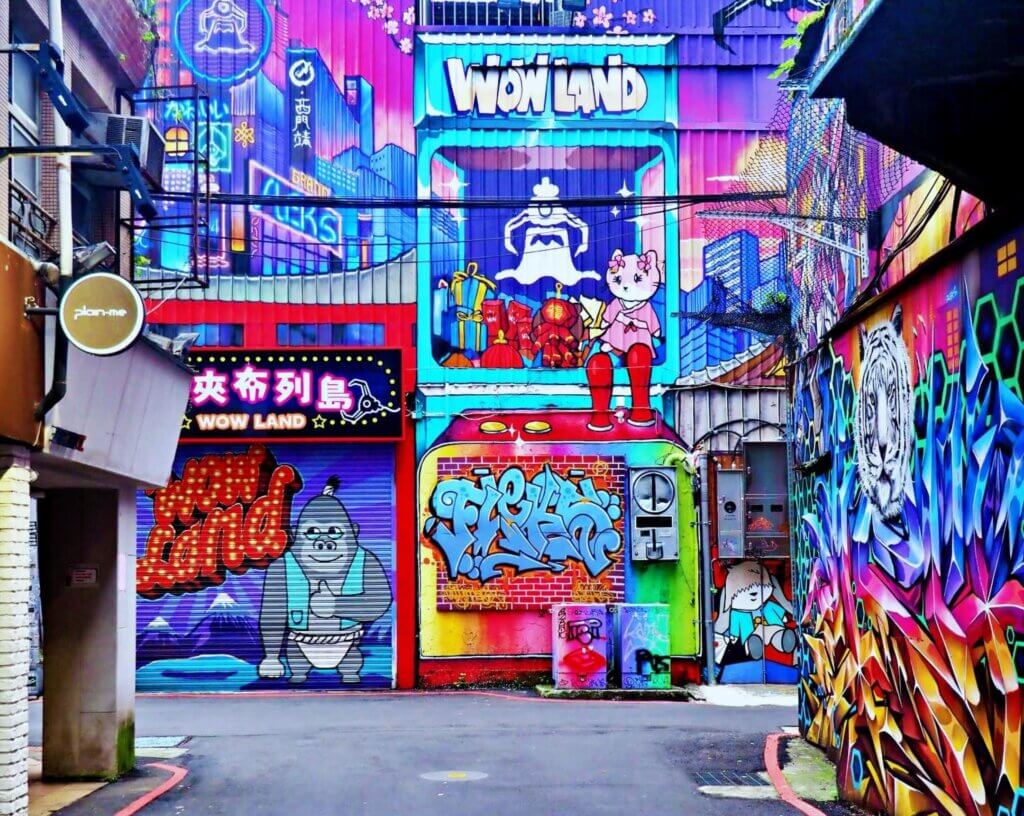 A colorful graffiti is painted on the wall of a building at an intersection between two alleys.