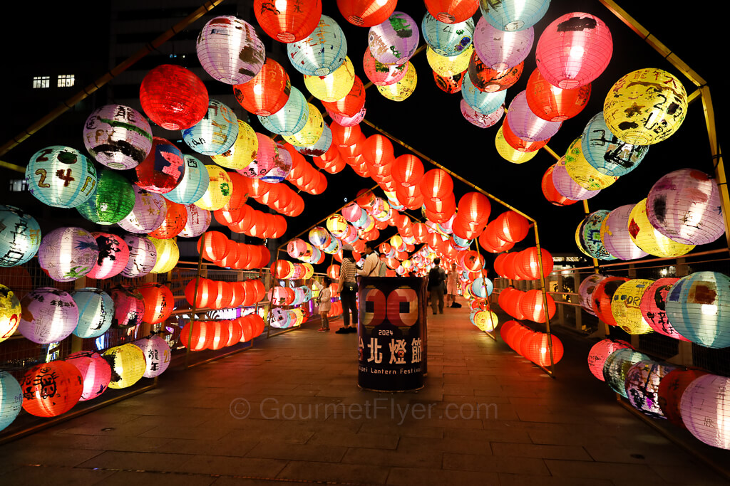 Many colorful lanterns are arranged above a bridge in a semi-circle formation.