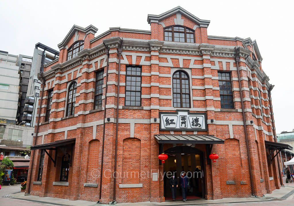 A two-story historical red brick building has a pair of red lanterns hanging above the front door.