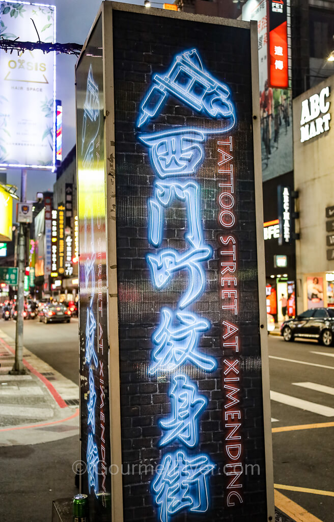 A tall vertical sign has the Chinese translation of tattoo street written in blue lighted characters.