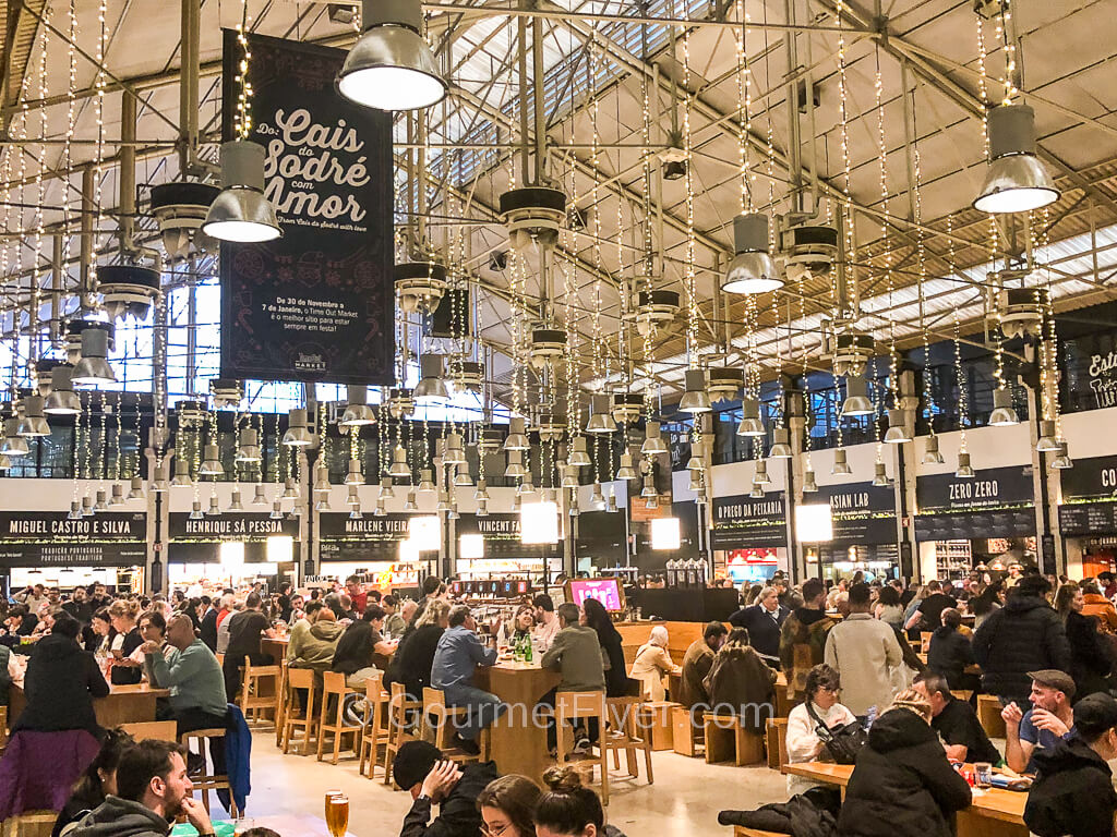 A lively and trendy food hall is packed with diners sitting at the bench like communal tables.